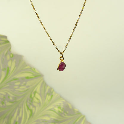 A delicate gold chain necklace with a small, rough-cut Pink Tourmaline gemstone pendant