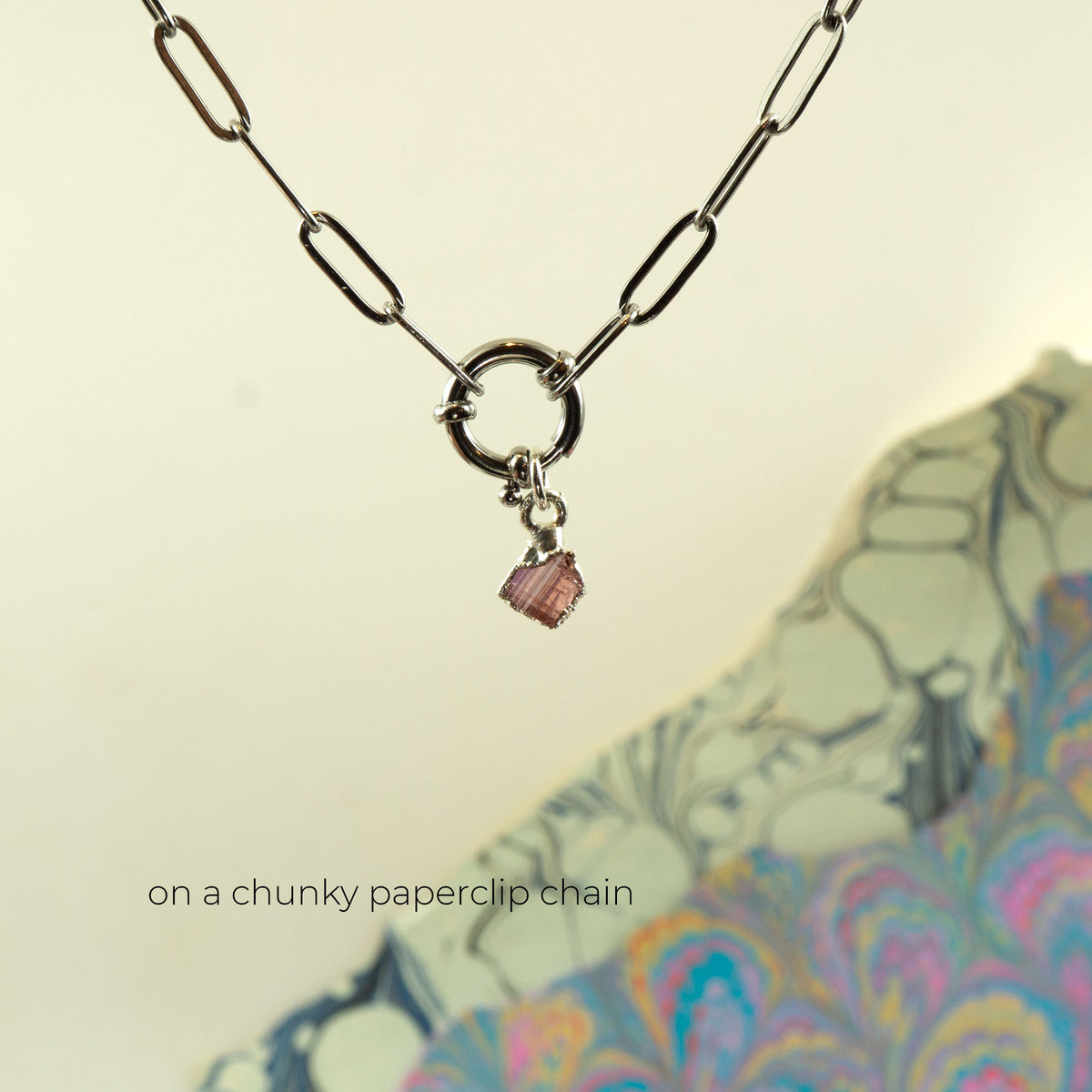 A silver-toned paperclip chain necklace with a circular ring clasp and a small Pink Tourmaline faceted gemstone charm