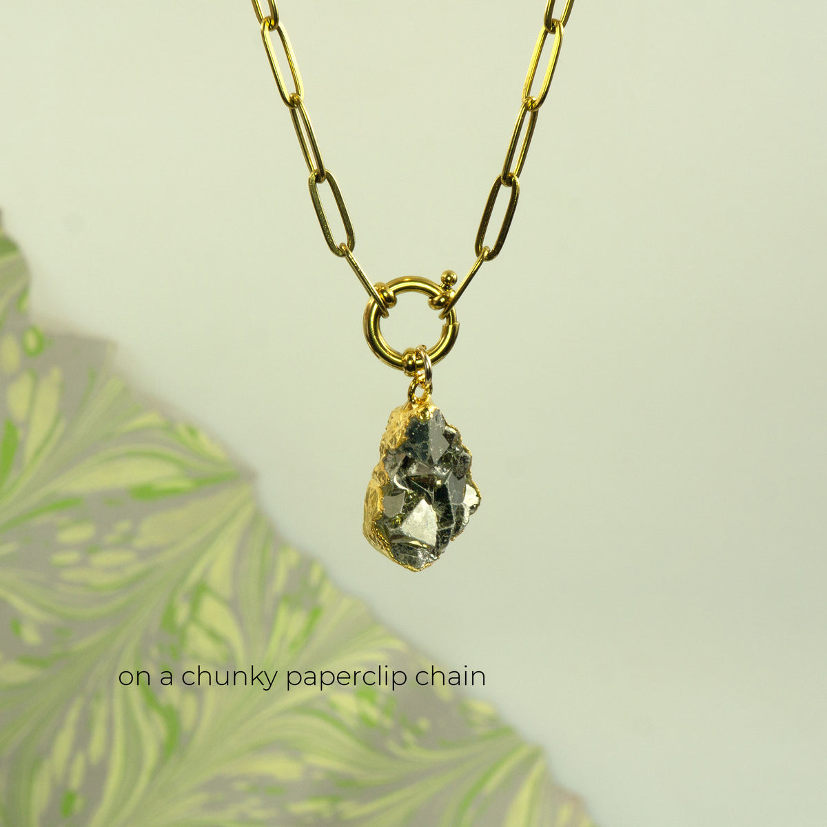 A gold paperclip chain necklace with a raw, chunky Pyrite gemstone pendant