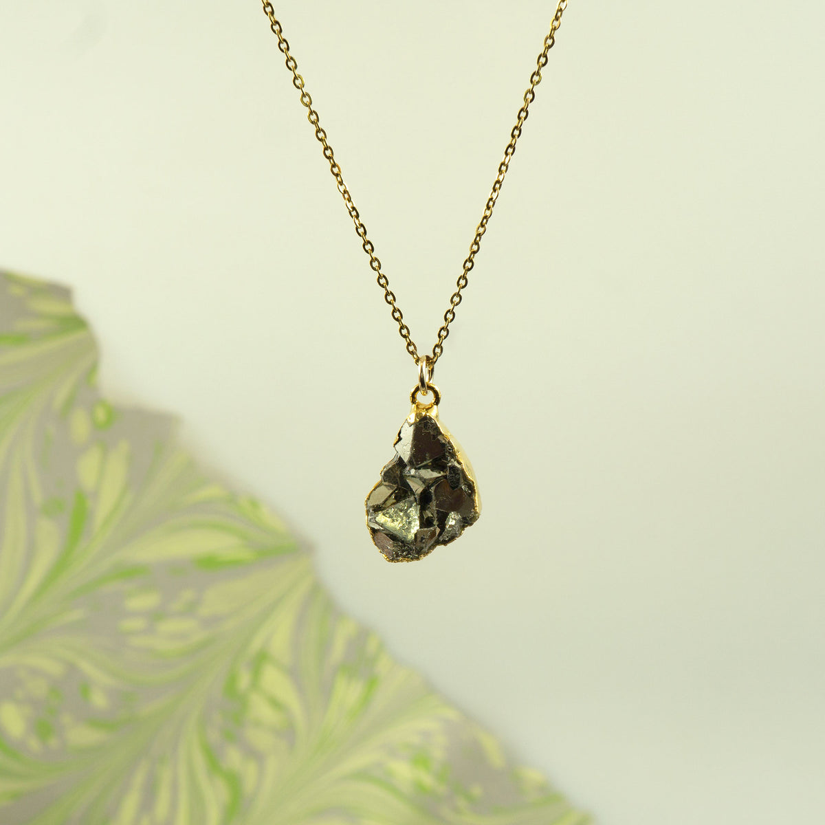 A gold chain necklace with a raw, faceted Pyrite gemstone pendant