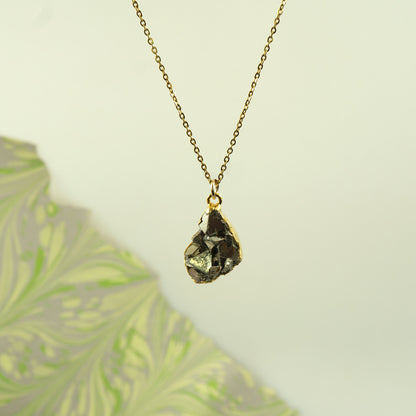 A gold chain necklace with a raw, faceted Pyrite gemstone pendant