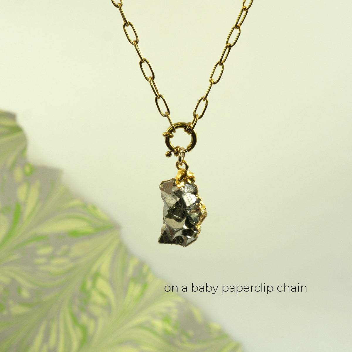 A gold paperclip chain necklace with a raw, rough metallic pyrite gemstone pendant