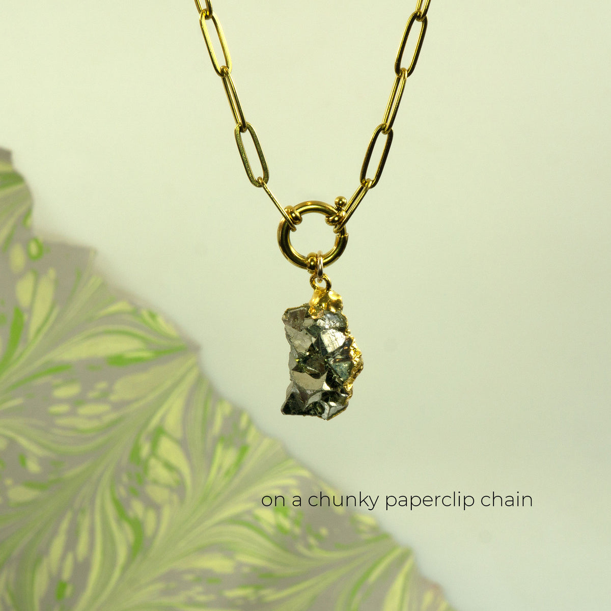 A gold paperclip chain necklace with a raw, metallic pyrite gemstone pendant