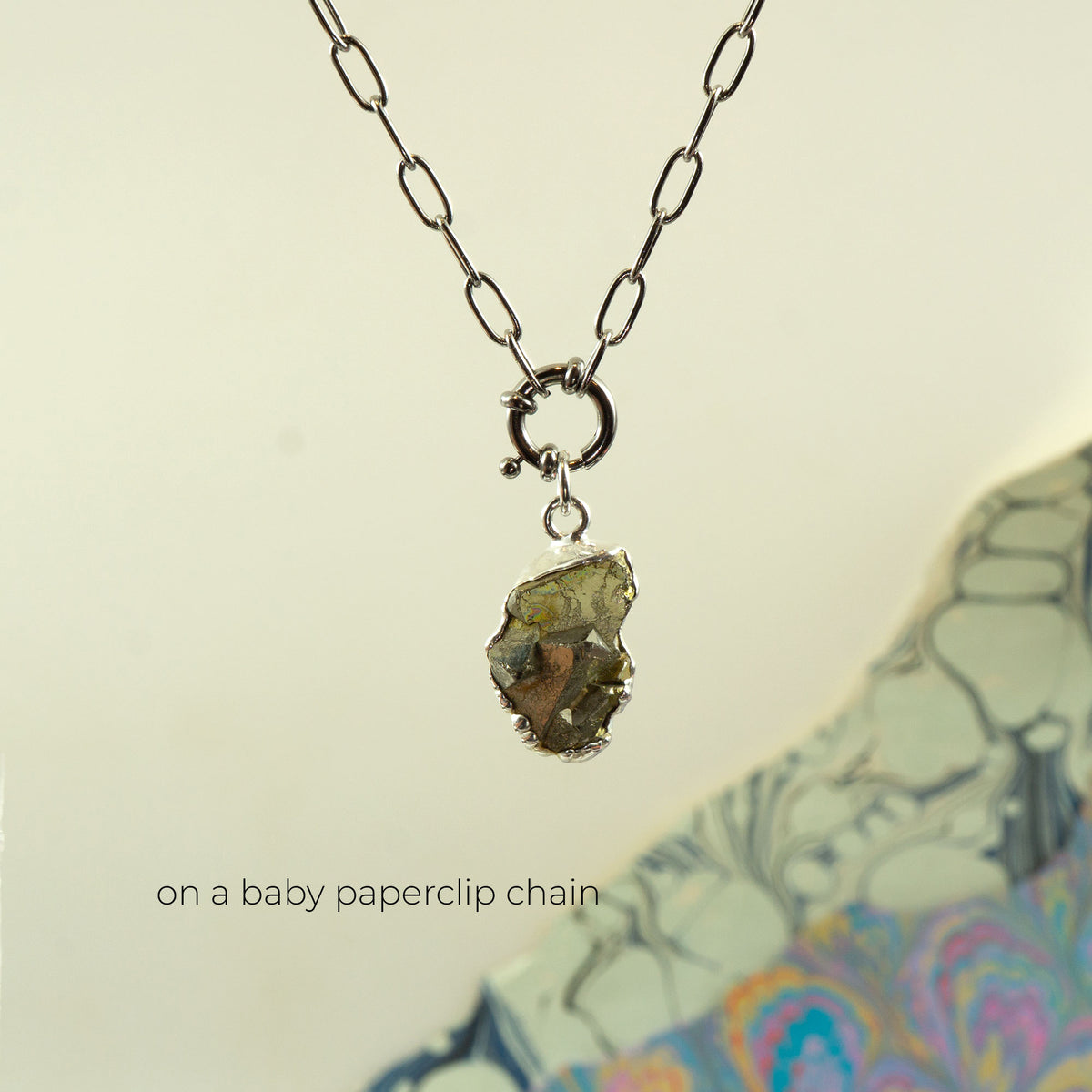 A necklace with a baby silver paperclip chain and a raw, rough,metallic pyrite gemstone pendant