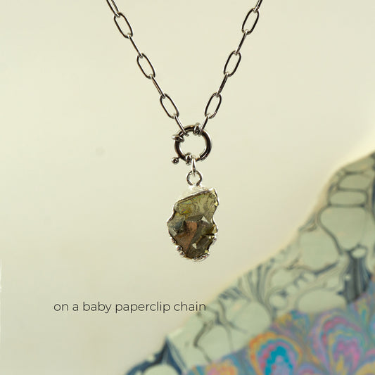 A necklace with a baby silver paperclip chain and a raw, rough,metallic pyrite gemstone pendant
