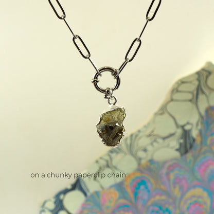 A necklace with a chunky silver paperclip chain and a raw, rough pyrite gemstone pendant