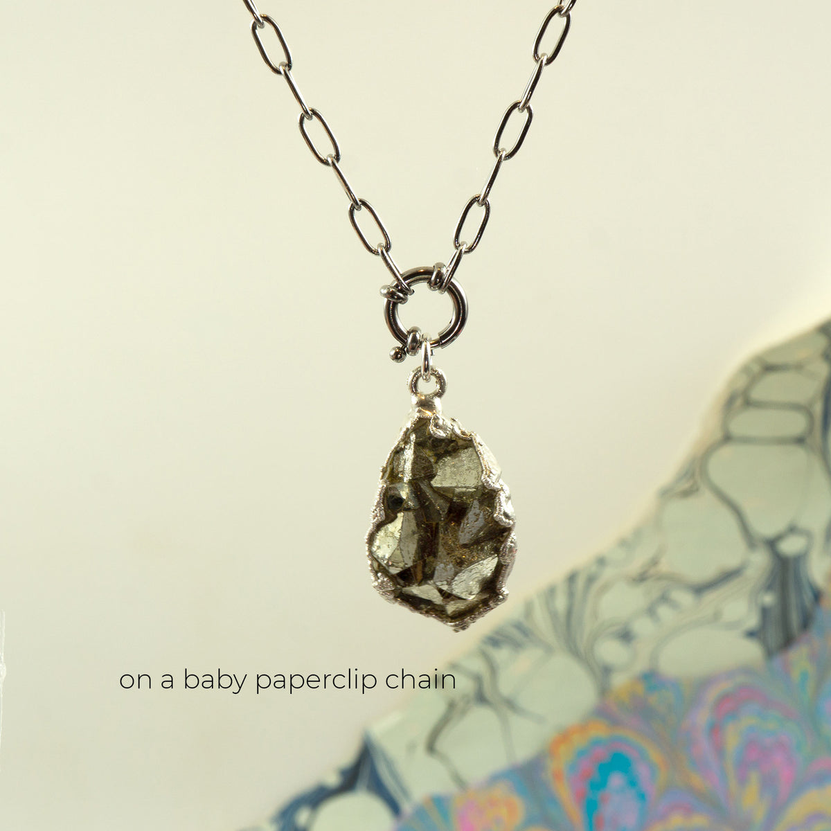 A silver paperclip chain necklace with a raw, faceted pyrite crystal pendant