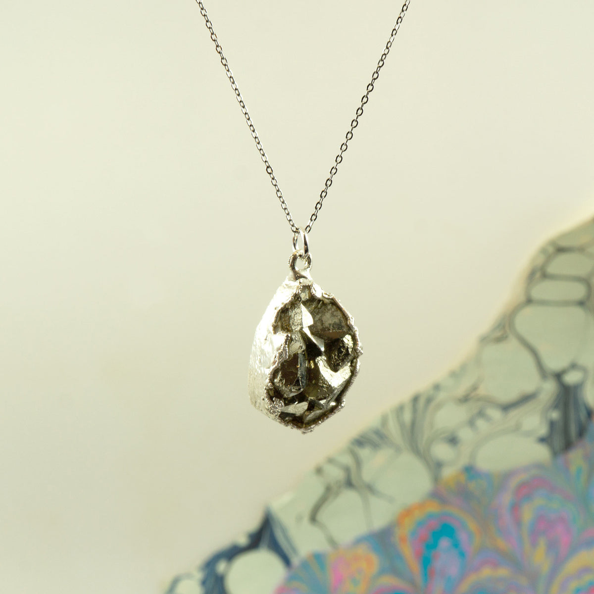 A silver necklace with a raw, textured teardrop-shaped pyrite pendant