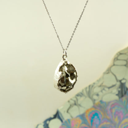 A silver necklace with a raw, textured teardrop-shaped pyrite pendant