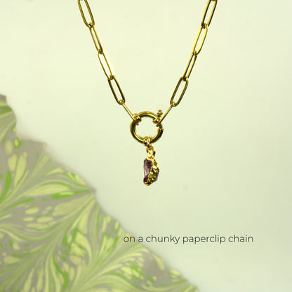 A gold paperclip chain necklace with a toggle clasp and a small dangling rhodlite garnet gemstone charm
