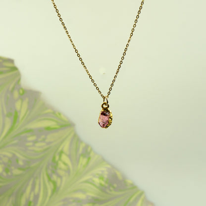 A delicate gold chain necklace with a small gold bezel holding a faceted pink rhodlite garnet gemstone pendant
