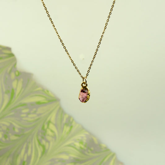 A delicate gold chain necklace with a small gold bezel holding a faceted pink rhodlite garnet gemstone pendant