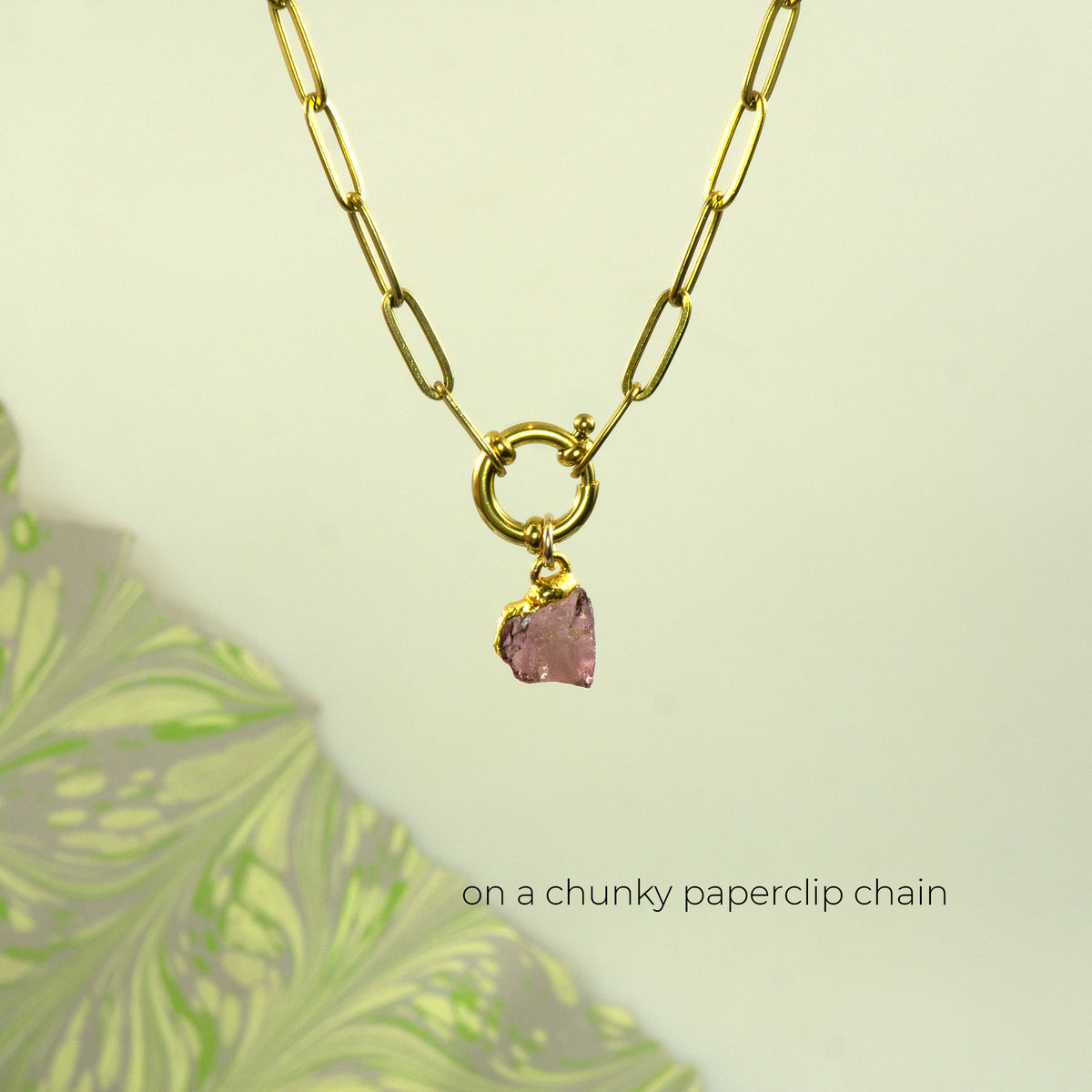 A gold paperclip chain necklace with a toggle clasp and a small faceted pink rhodolite garnet gemstone pendant