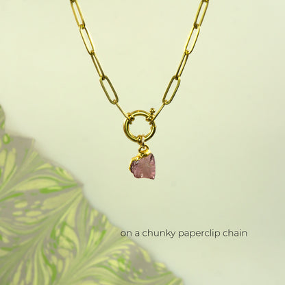 A gold paperclip chain necklace with a toggle clasp and a small faceted pink rhodolite garnet gemstone pendant