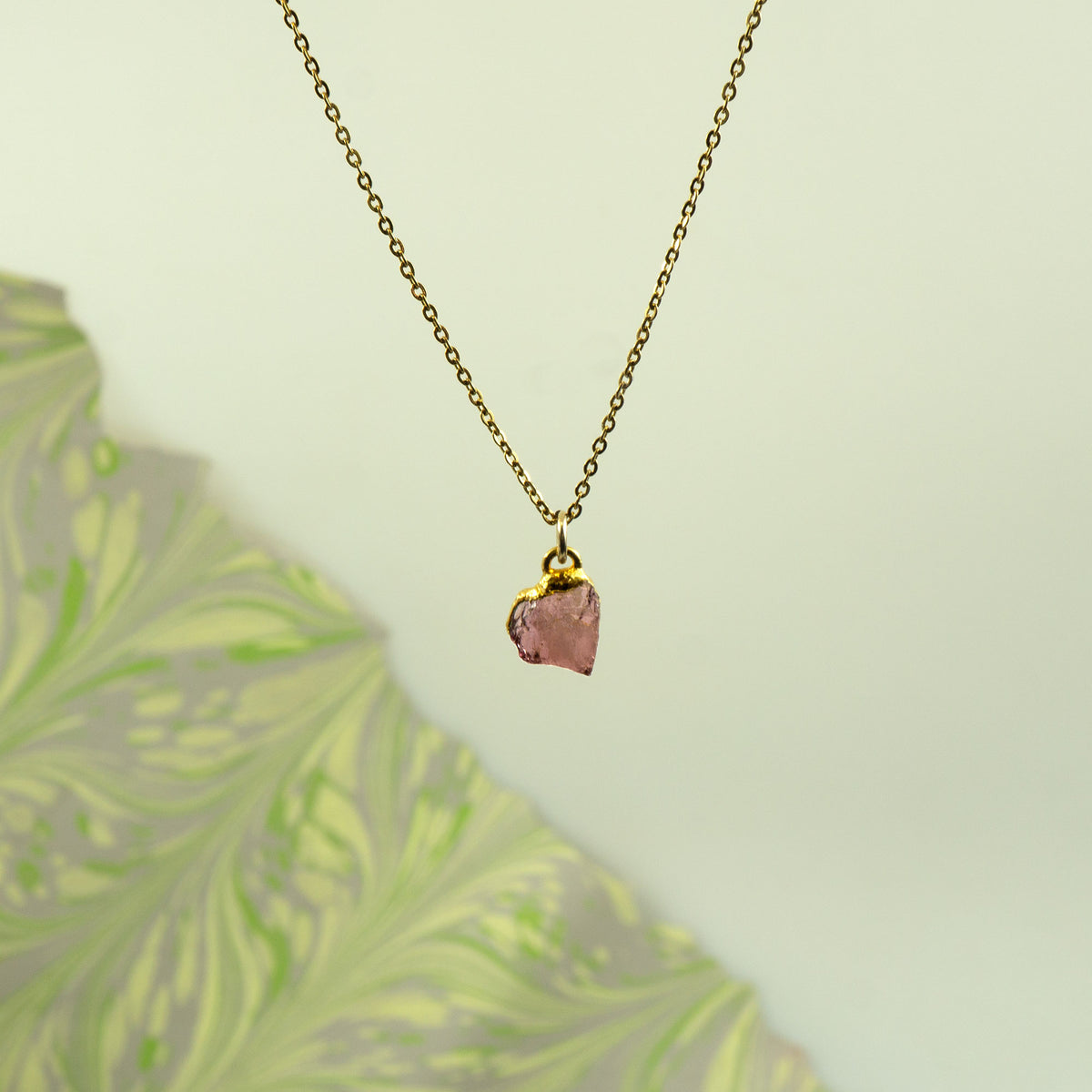 A delicate gold chain necklace with a raw, irregular pink rhodolite garnet stone pendant