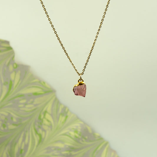 A delicate gold chain necklace with a raw, irregular pink rhodolite garnet stone pendant