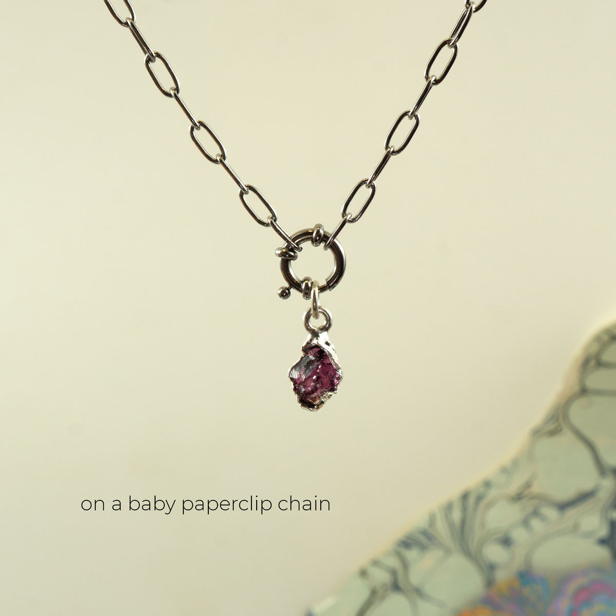 A silver paperclip chain necklace with a small silver ring clasp and a dangling faceted pink rhodolite garnet gemstone pendant
