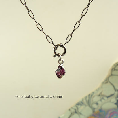 A silver paperclip chain necklace with a small silver ring clasp and a dangling faceted pink rhodolite garnet gemstone pendant