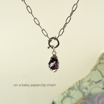 A silver paperclip chain necklace with a small ring clasp holding a rough, irregular dark purple rhodolite-garnet gemstone pendant
