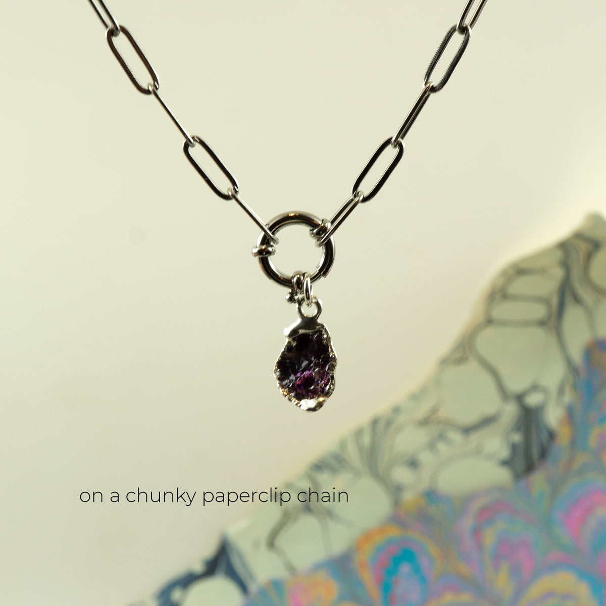 A silver paperclip chain necklace with a ring clasp holding a raw, irregular purple rhodolite-garnet gemstone pendant
