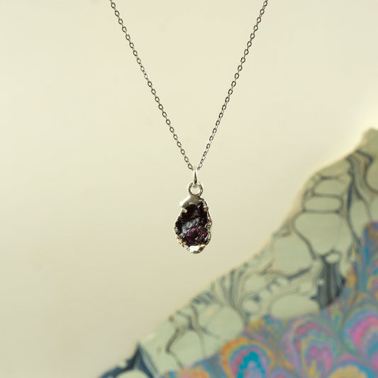 A silver chain necklace with a raw, polished dark purple rhodolite-garnet crystal pendant