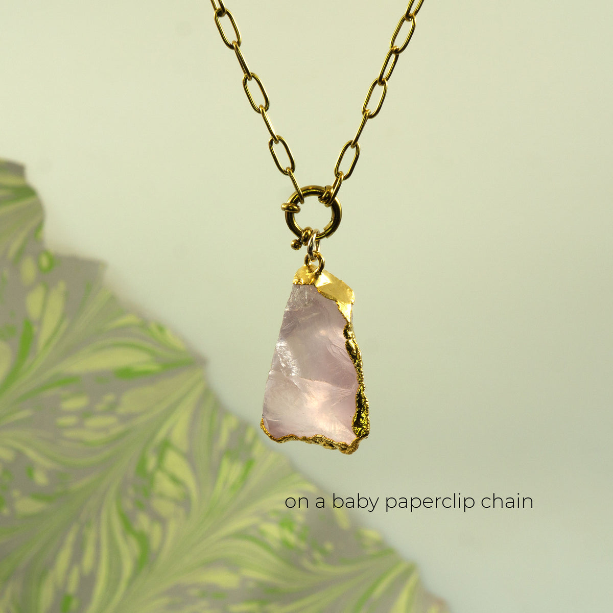 A raw pink rose quartz crystal pendant on a gold baby paperclip chain necklace.