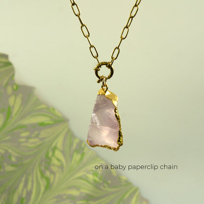 A raw pink rose quartz crystal pendant on a gold baby paperclip chain necklace.