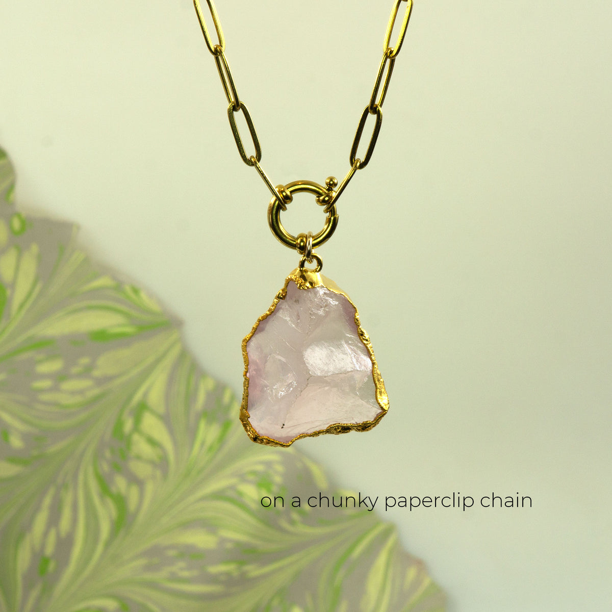 A gold chunky paperclip chain necklace with a raw, irregular pale pink rose quartz stone pendant