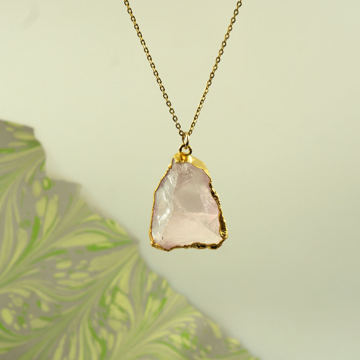 A gold chain necklace with a raw, irregular-cut pale pink rose quartz stone pendant