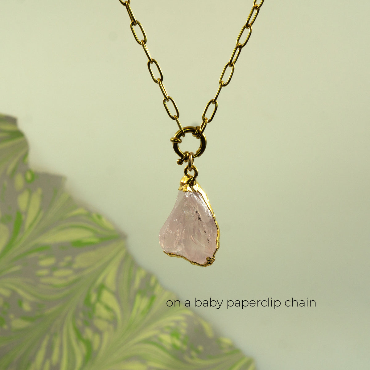 A gold baby paperclip chain necklace with a raw, irregular-cut pale pink raw quartz stone pendant.