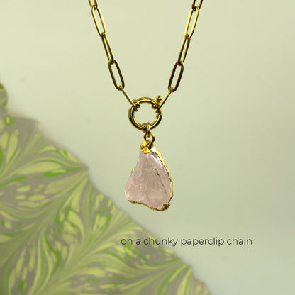 A gold paperclip chain necklace with a raw, irregularly shaped pale pink rose quartz pendant