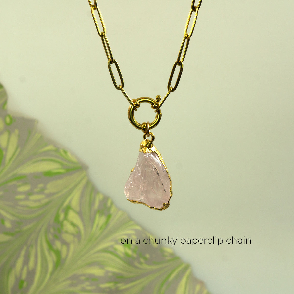 A gold chunky paperclip chain necklace with a raw, irregularly shaped pale pink rose quartz stone pendant