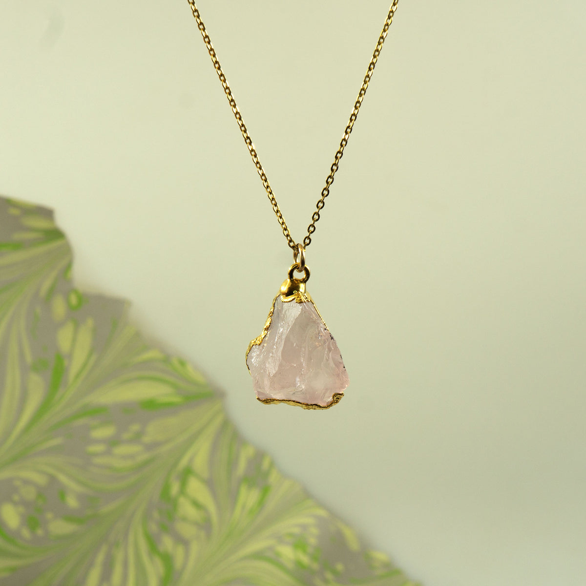 A gold chain necklace with a raw, irregular-cut pale pink rose quartz crystal pendant
