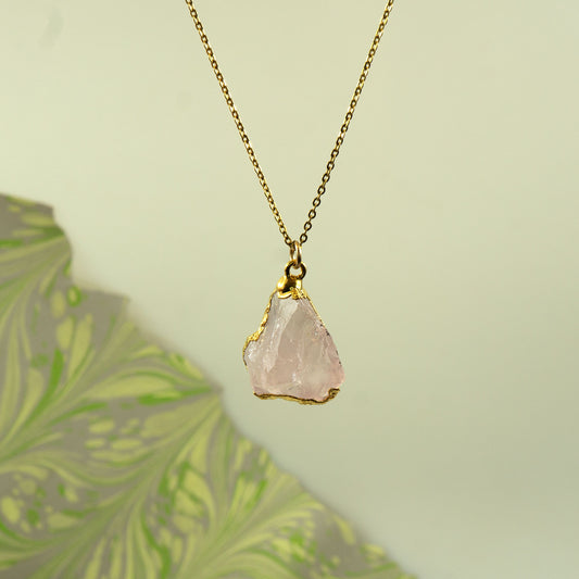 A gold chain necklace with a raw, irregular-cut pale pink rose quartz crystal pendant