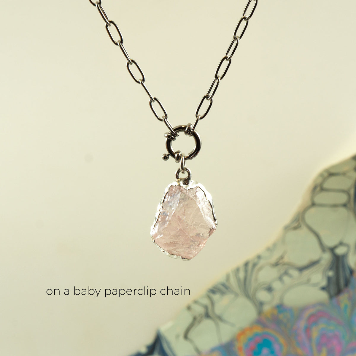 A necklace with a faceted pale pink rose quartz gemstone pendant on a silver paperclip chain