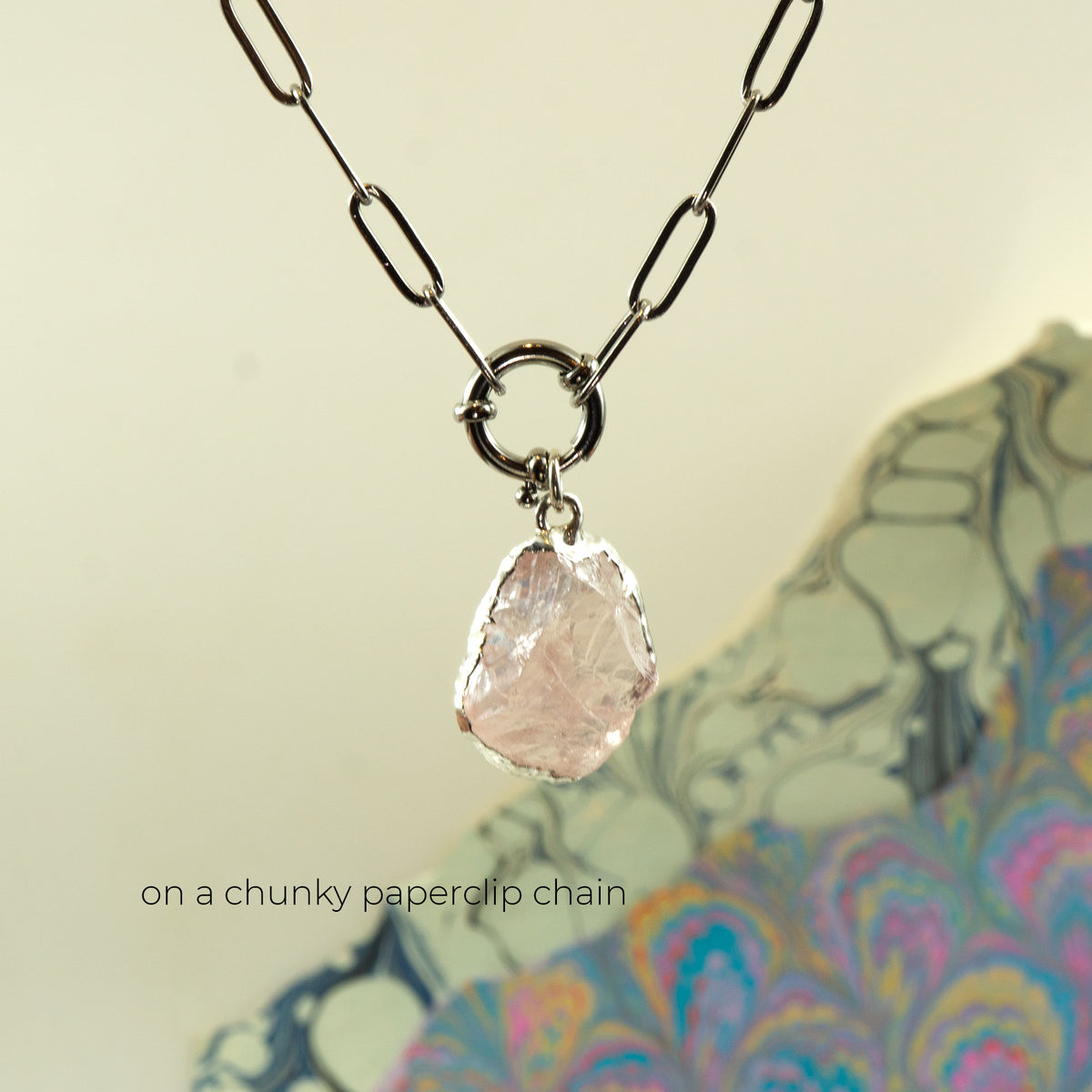 A necklace with a chunky metal chain and a raw, irregular pale pink rose quartz stone pendant