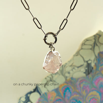 A necklace with a chunky metal chain and a raw, irregular pale pink rose quartz stone pendant
