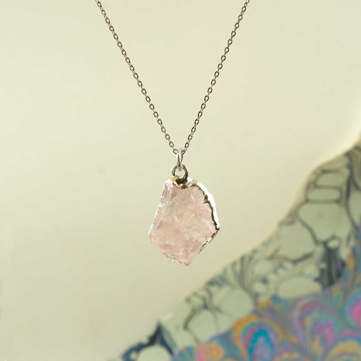 A silver chain necklace with a raw, irregular-cut pale rose quartz crystal pendant