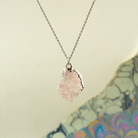 A silver chain necklace with a raw, irregular-cut pale rose quartz crystal pendant