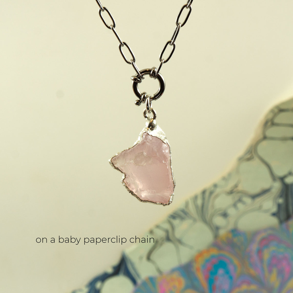 A silver paperclip chain necklace with a raw, irregular-shaped light pink Rose Quartz stone pendant