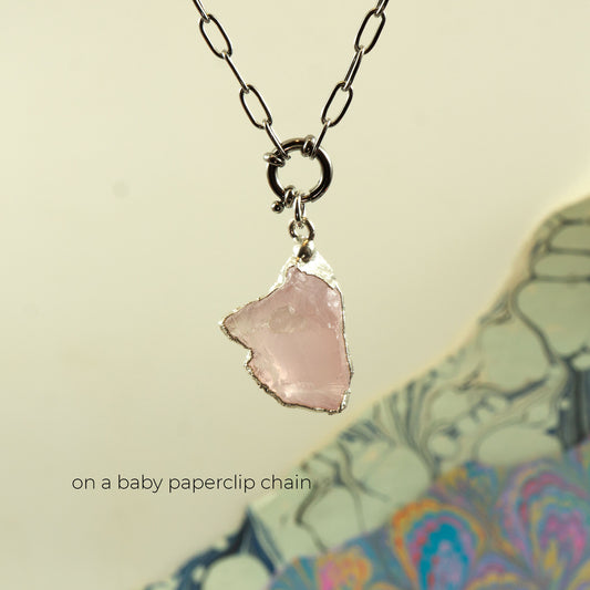 A silver paperclip chain necklace with a raw, irregular-shaped light pink Rose Quartz stone pendant