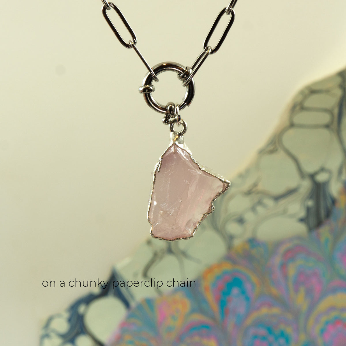 A silver paperclip chain necklace with a raw, irregular-cut light pink Rose Quartz stone pendant