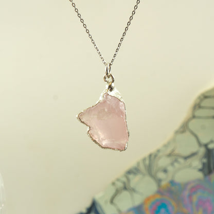 A silver chain necklace featuring a raw, irregular-shaped light pink Rose Quartz stone pendant with rough silver edges