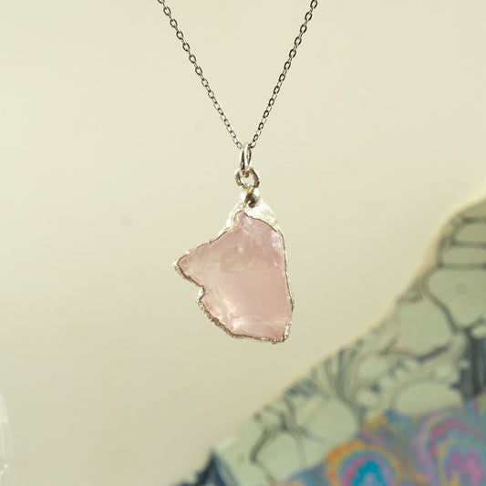 A silver chain necklace featuring a raw, irregular-shaped light pink Rose Quartz stone pendant with rough silver edges