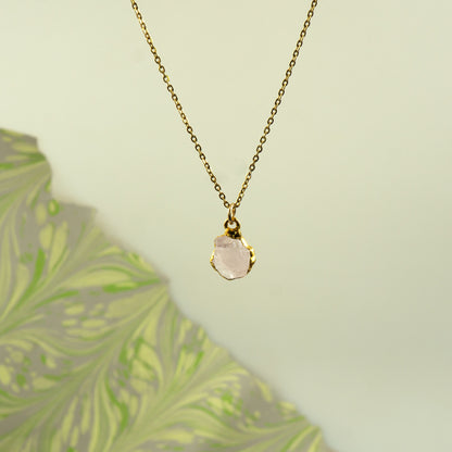 A delicate gold chain necklace with a raw, irregular-cut pale pink rose quartz stone pendant