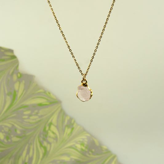 A delicate gold chain necklace with a raw, irregular-cut pale pink rose quartz stone pendant