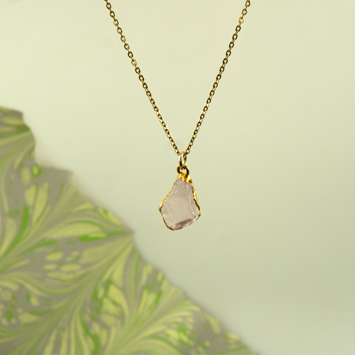 A gold chain necklace with a raw, irregular-cut pale pink rose quartz gemstone pendant