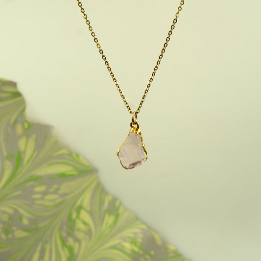 A gold chain necklace with a raw, irregular-cut pale pink rose quartz gemstone pendant