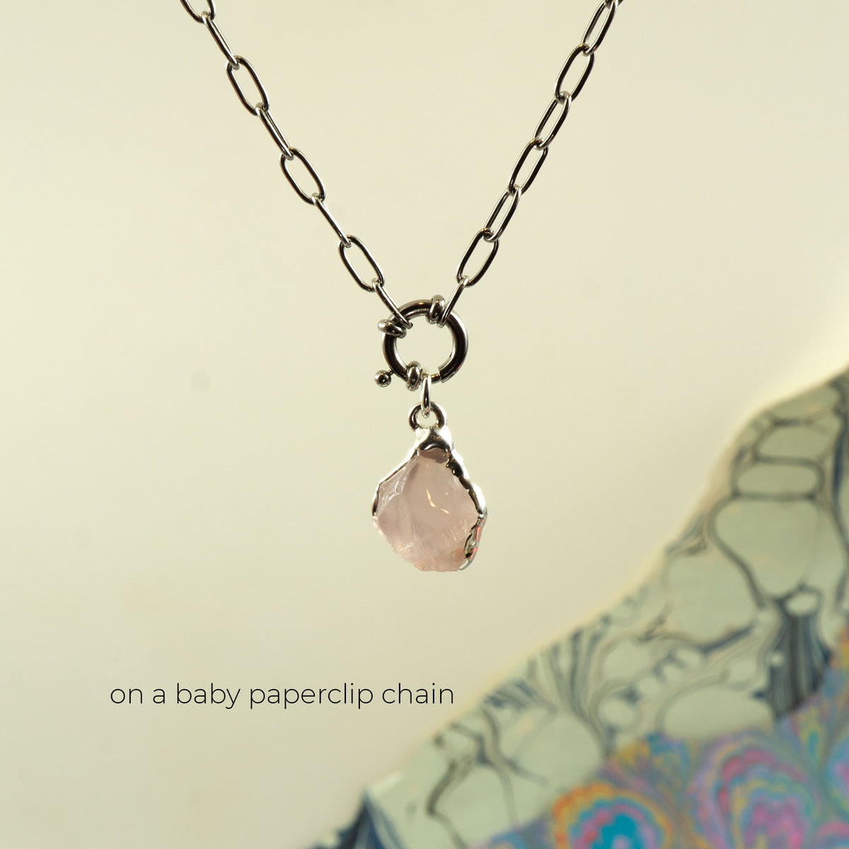 A silver paperclip chain necklace with a small ring clasp holding a faceted pale pink rose quartz gemstone pendant