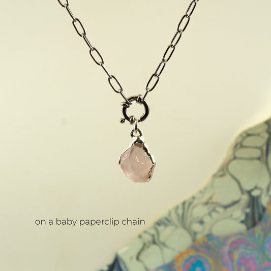 A silver paperclip chain necklace with a small ring clasp holding a faceted pale pink rose quartz gemstone pendant